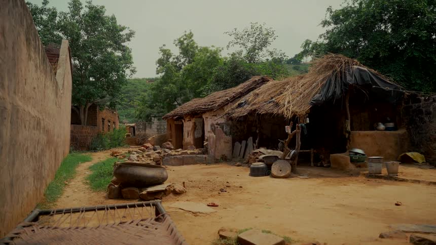 A static wide shot of traditional mud huts with thatched roofs in a rural village in India