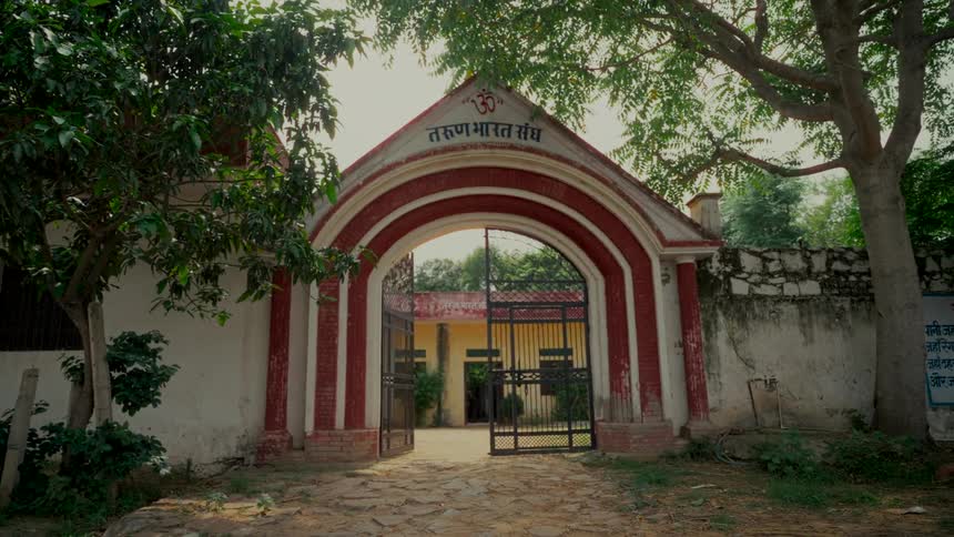 Static shot of the arched entrance gate of the Tarun Bharat Sangh building in rural India, featuring Hindi script and an Om symbol