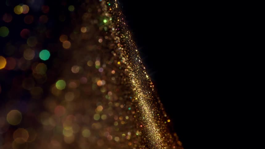 A stream of shimmering gold glitter particles flows diagonally with a beautiful bokeh effect against a dark background
