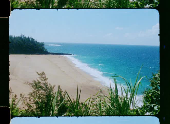A vintage film shot captures a scenic high-angle view of a tropical sandy beach with turquoise ocean waves rolling in