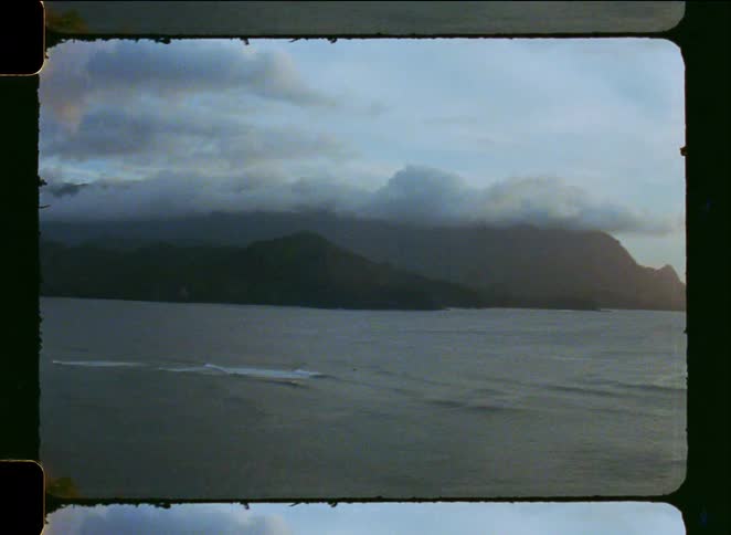 A vintage film pan reveals the sun breaking through the clouds over a dramatic mountain coastline