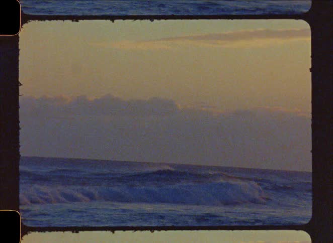A grainy super 8mm film shot captures ocean waves breaking during a peaceful sunrise
