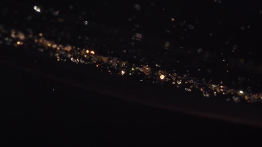 A macro shot of shimmering golden glitter particles slowly drifting through a dark void