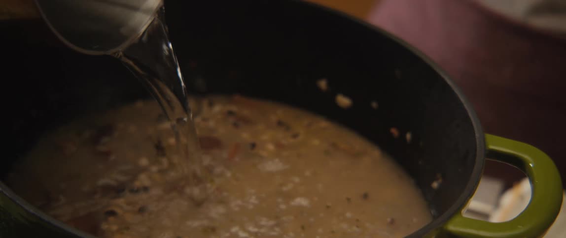 A close-up slow-motion shot of water being poured into a pot of cooking black-eyed peas