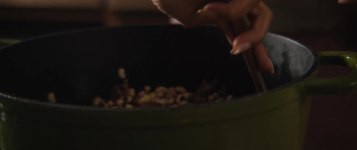 A close-up slow-motion shot of a person stirring a pot of black-eyed peas and seasonings with a wooden spoon