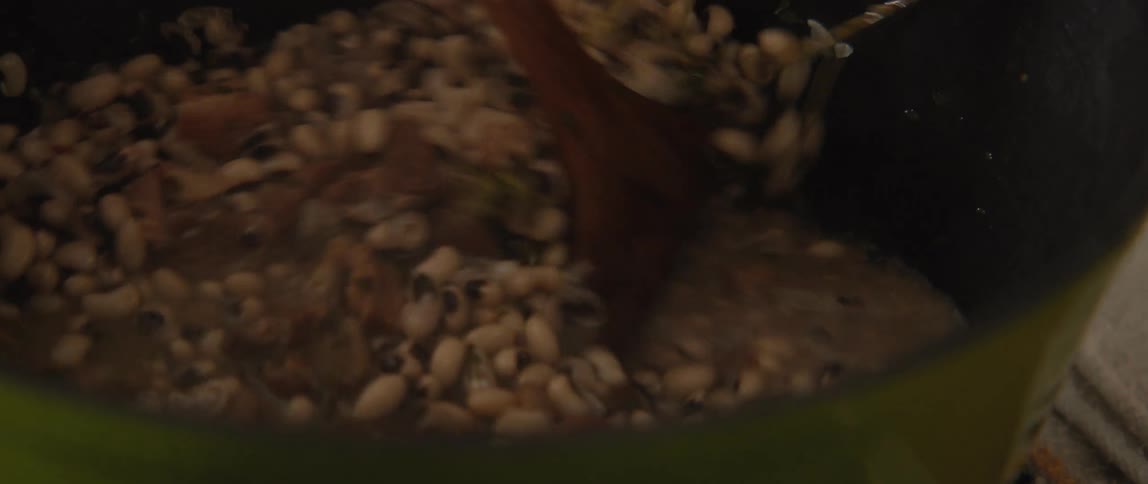 A slow-motion close-up shot of a hearty pot of black-eyed peas being stirred with a wooden spoon