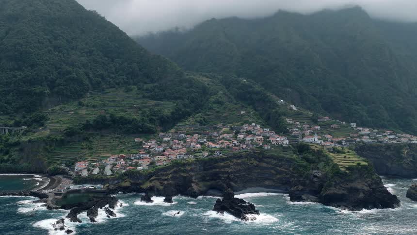 A stunning aerial view of the picturesque coastal village of Seixal, Madeira, nestled into lush green mountainsides on a foggy day