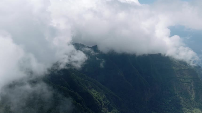 A breathtaking aerial view of lush green mountain peaks disappearing into a thick blanket of slow-moving clouds