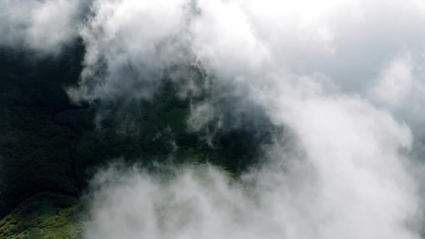 An ethereal aerial view looking down through soft white clouds onto a lush green mountain landscape