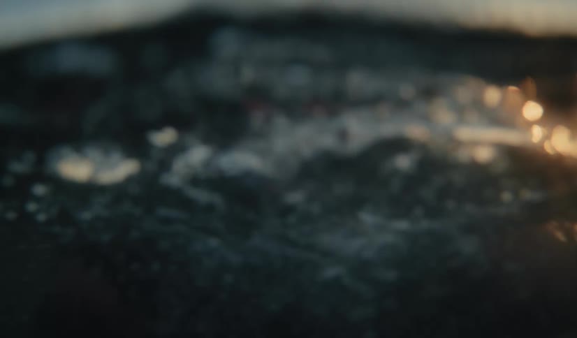 A dramatic slow-motion shot of a woman emerging from the ocean at sunset, gasping for air in an emotional release