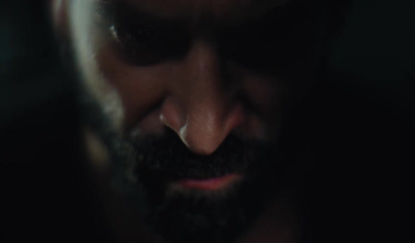 Extreme close-up of a tormented man's face as he shakes with rage and looks up with a sinister stare in the dark