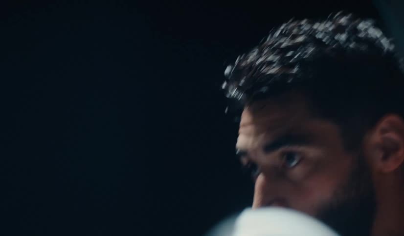 Intense close-up of a muscular male boxer shadowboxing against a black background
