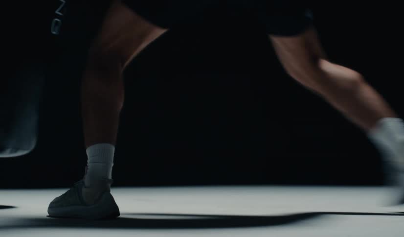 A boxer trains with a punching bag in a dark studio, with slow-motion close-ups on their agile footwork and powerful punches