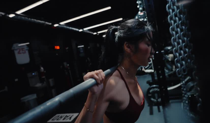 Slow motion side view of a determined woman performing a heavy barbell squat in a dark, atmospheric gym