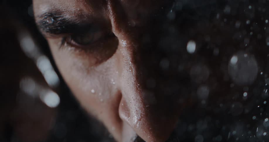 Extreme close-up of a man's solemn face as rain falls on him in dramatic slow motion