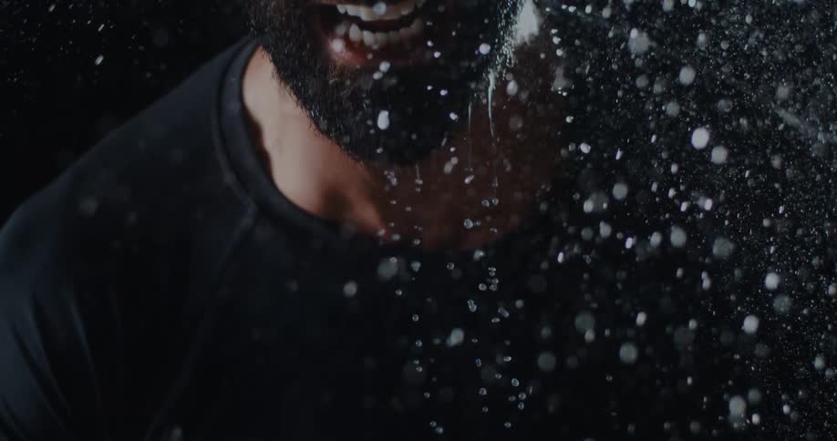Dramatic super slow motion close-up of a bearded man screaming as water rains down on him