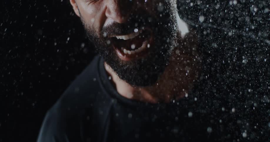 Dramatic slow motion close up of a bearded man screaming in the rain