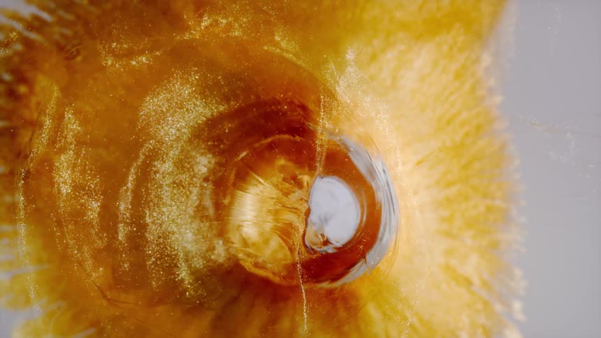 Mesmerizing macro shot of golden glitter particles creating a hypnotic swirling vortex in liquid