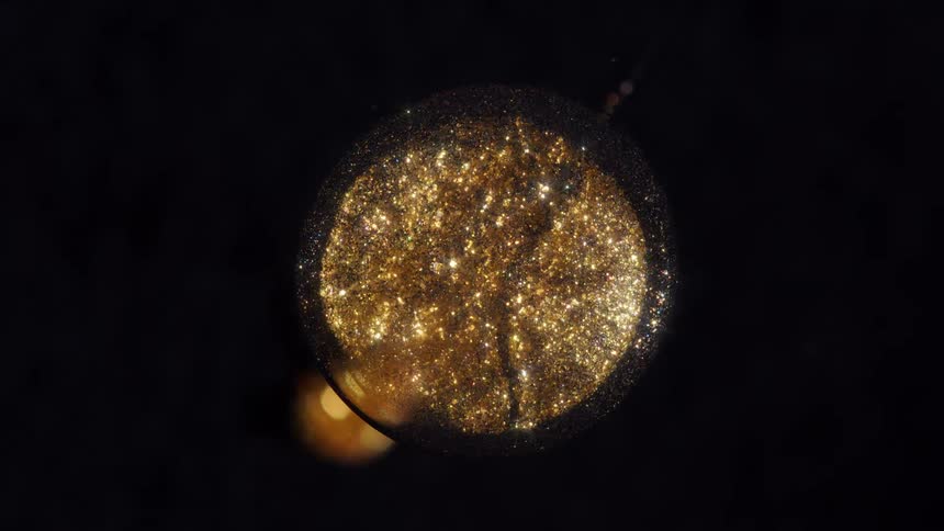 A macro view of a swirling golden galaxy of glitter inside a glass sphere against a dark background