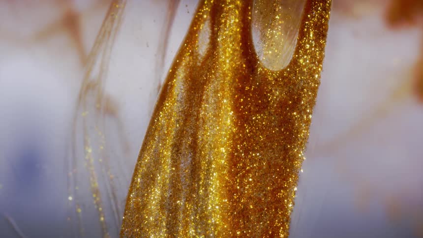 A shimmering river of golden glitter slowly flows in a viscous liquid in this abstract macro shot