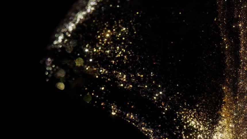 An elegant and mesmerizing river of shimmering gold glitter flows and swirls against a dark background