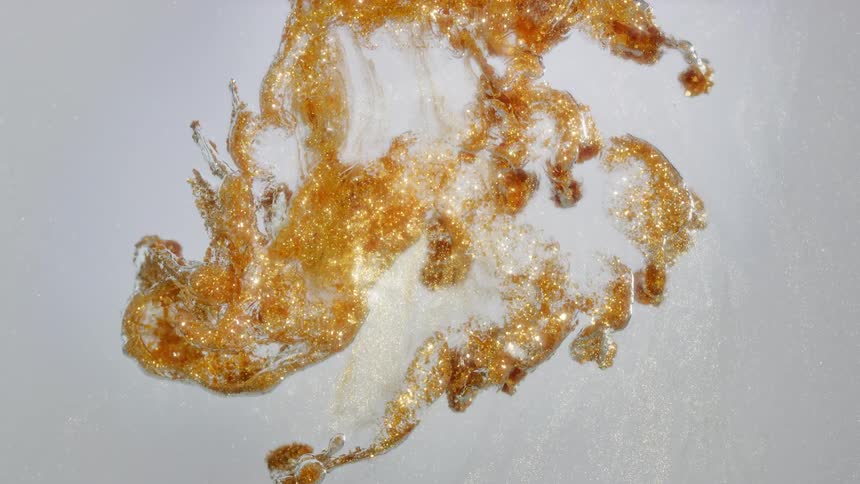 Sparkling gold and amber colors mix and flow in a white liquid, creating an elegant abstract background