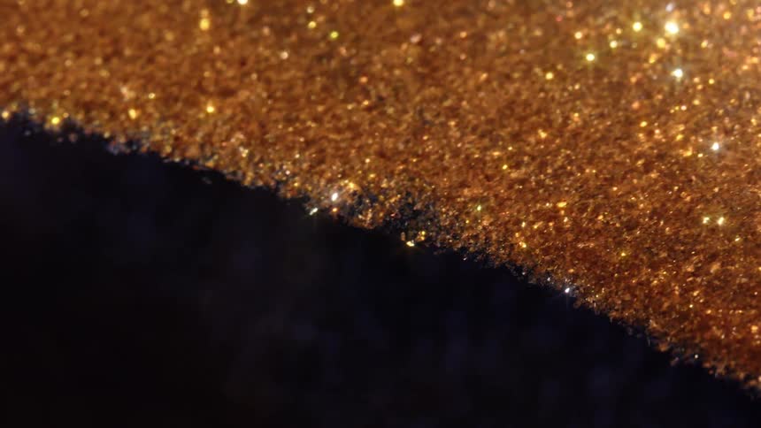 An extreme close-up, slow pan shot of a sparkling golden glitter surface against a dark, contrasting background