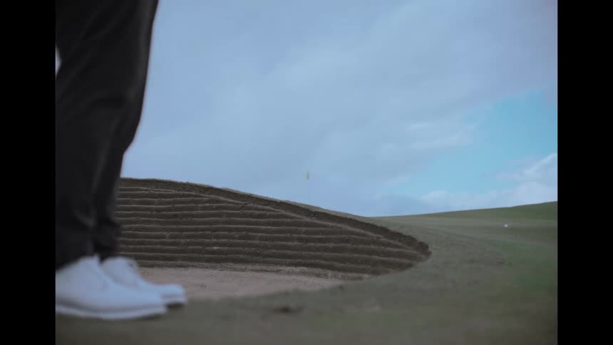 A golfer hits a golf ball out of a sand trap in slow motion on a beautiful golf course