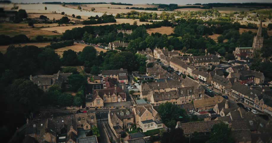 A serene, static high-angle aerial view of a classic English town with stone houses and lush green countryside