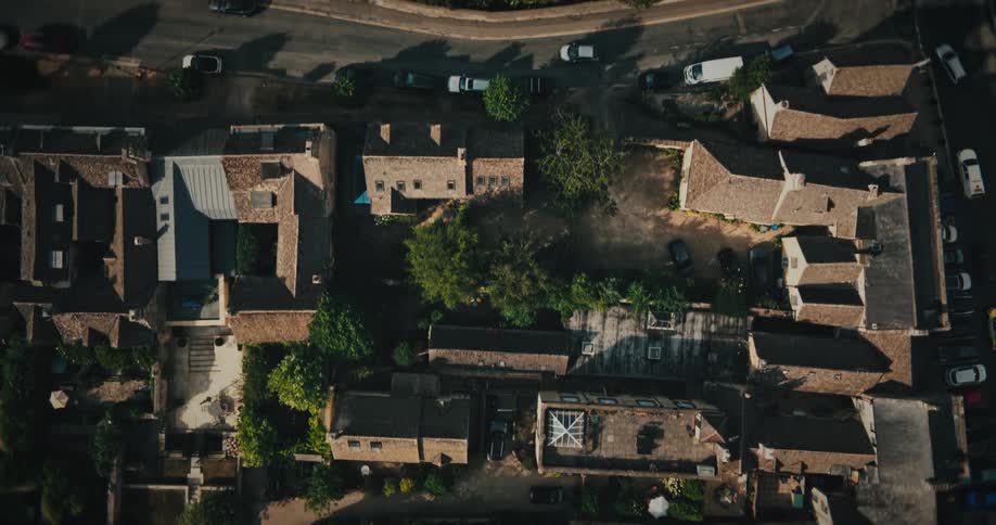 Aerial bird's-eye-view slowly ascending over the rooftops of a quaint, historic European village on a sunny day