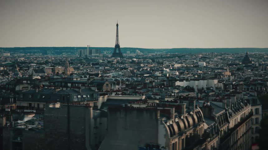 A cinematic aerial view tracks sideways over the classic rooftops of Paris with the Eiffel Tower on the distant skyline