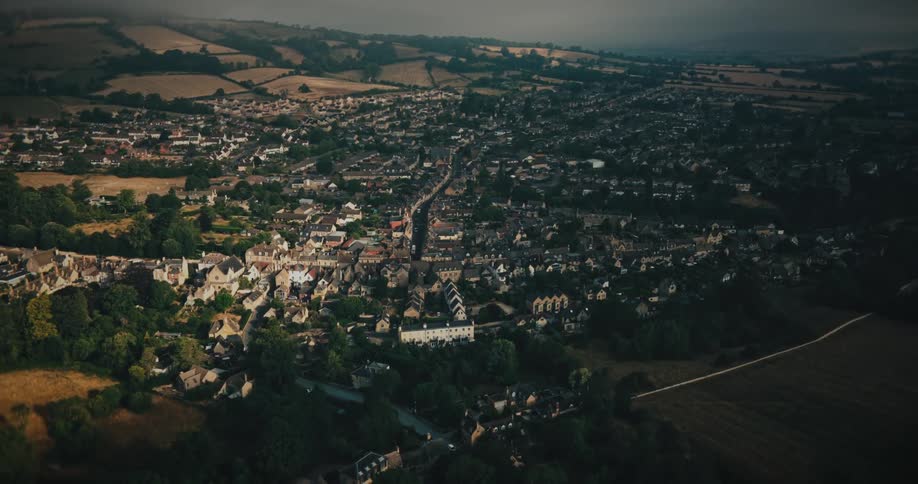 A slow cinematic aerial shot pulling back to reveal a historic English town nestled in the lush, rolling countryside