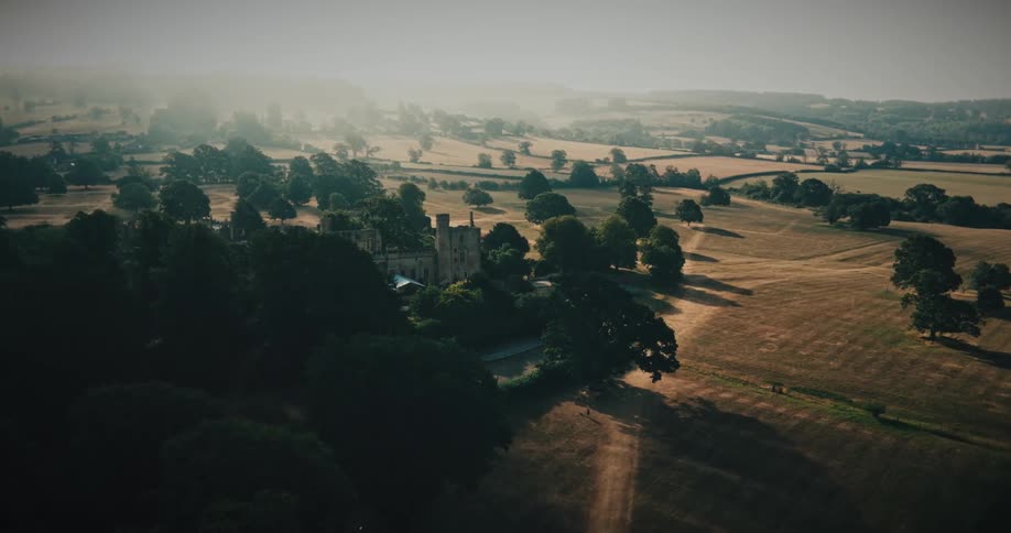 An aerial shot flies toward the majestic ruins of an ancient castle nestled in the hazy, rolling countryside