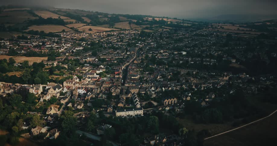 An atmospheric aerial view slowly approaches a picturesque English town nestled in the rolling countryside on an overcast day