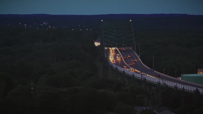 Aerial view of evening traffic flowing across a large green bridge surrounded by a dark forest