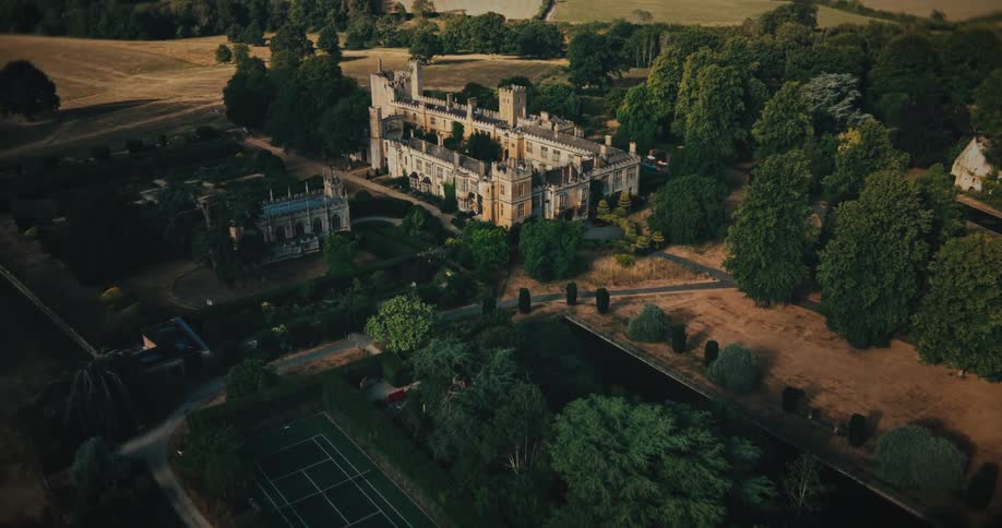 A dramatic aerial flight over the English countryside slowly reveals a majestic historic castle, culminating in a top-down view of its beautiful courtyard