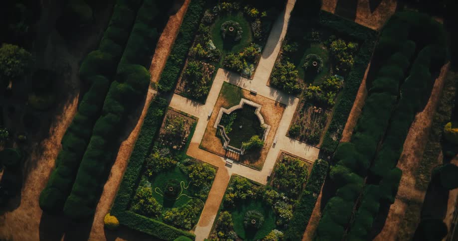 An elegant top-down aerial shot reveals the beautiful symmetry of a classic formal garden with manicured hedges and a central water feature