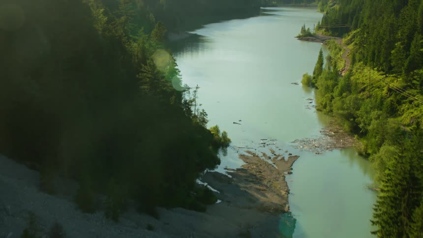 A river flows through a valley lined with pine trees