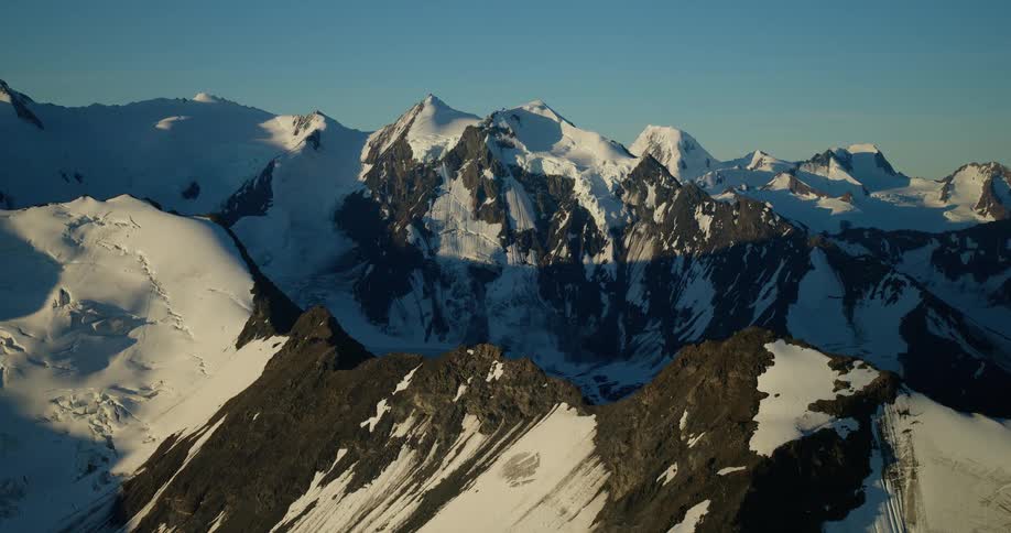 A cinematic aerial view slowly reveals the vast, snow-capped mountain range of the Alps during a golden sunrise