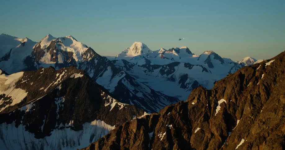 A small airplane soars over a majestic, snow-capped mountain range during a beautiful golden sunrise