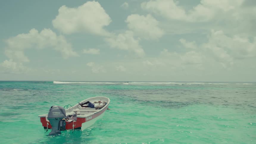 A man takes a peaceful nap in his small motorboat as it gently drifts on the beautiful turquoise sea