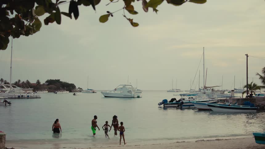 Local families and children enjoy a relaxing swim in a tranquil tropical harbor filled with moored boats