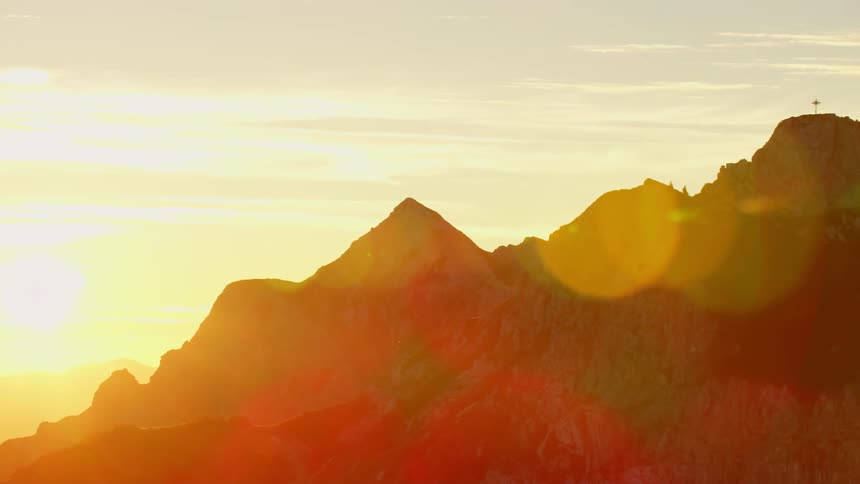 The sun rises behind jagged mountains