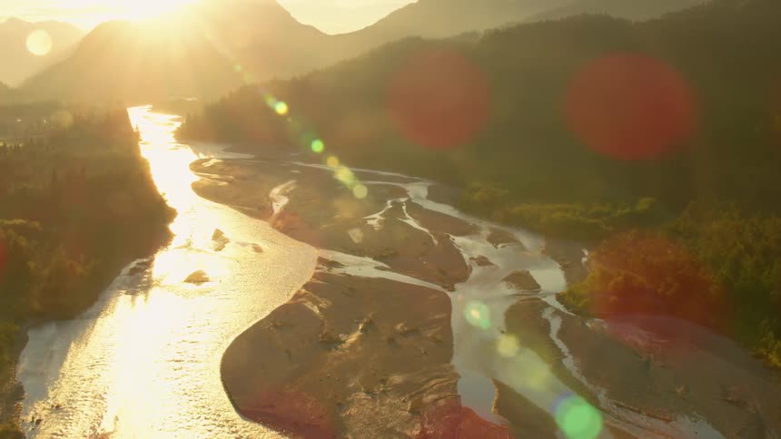 Aerial view moving down a river between mountains at sunset