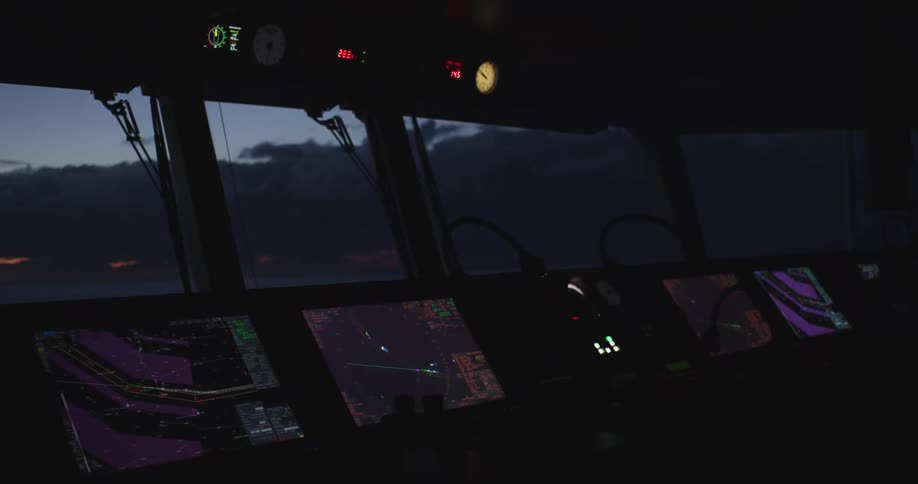 Advanced navigation equipment and control panels glow on the bridge of a large ship sailing the ocean at dusk