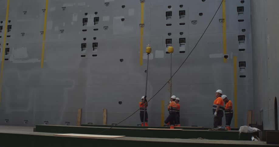 A team of industrial workers in safety gear prepares for a heavy lifting operation inside a massive factory