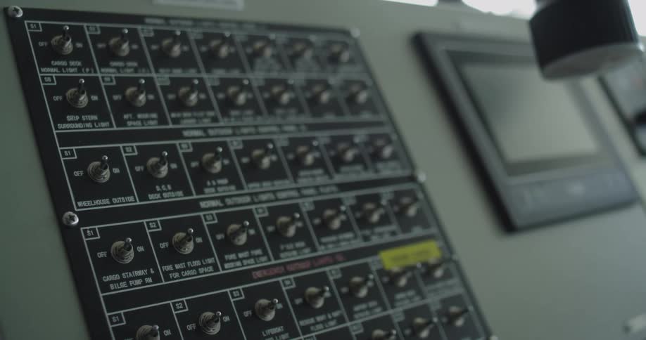 Close-up static shot of a dark control panel with numerous metal toggle switches for a large ship