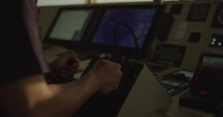 An officer operates the main engine control levers on the bridge of a large vessel