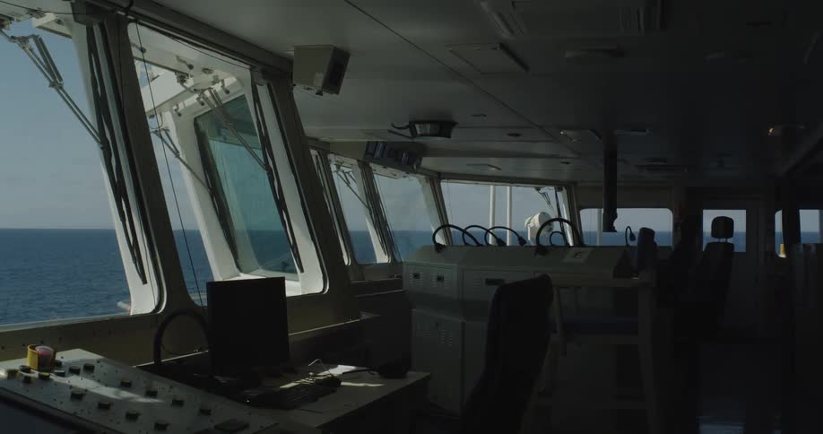 An empty ship's bridge navigates the calm, blue waters of the ocean on a bright day
