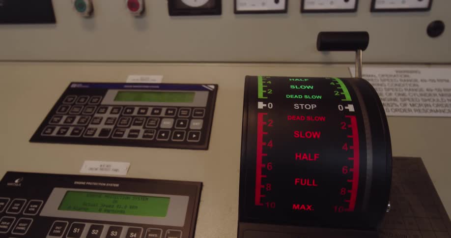 A close-up shot of the engine order telegraph lever and control panels in the engine room of a modern ship